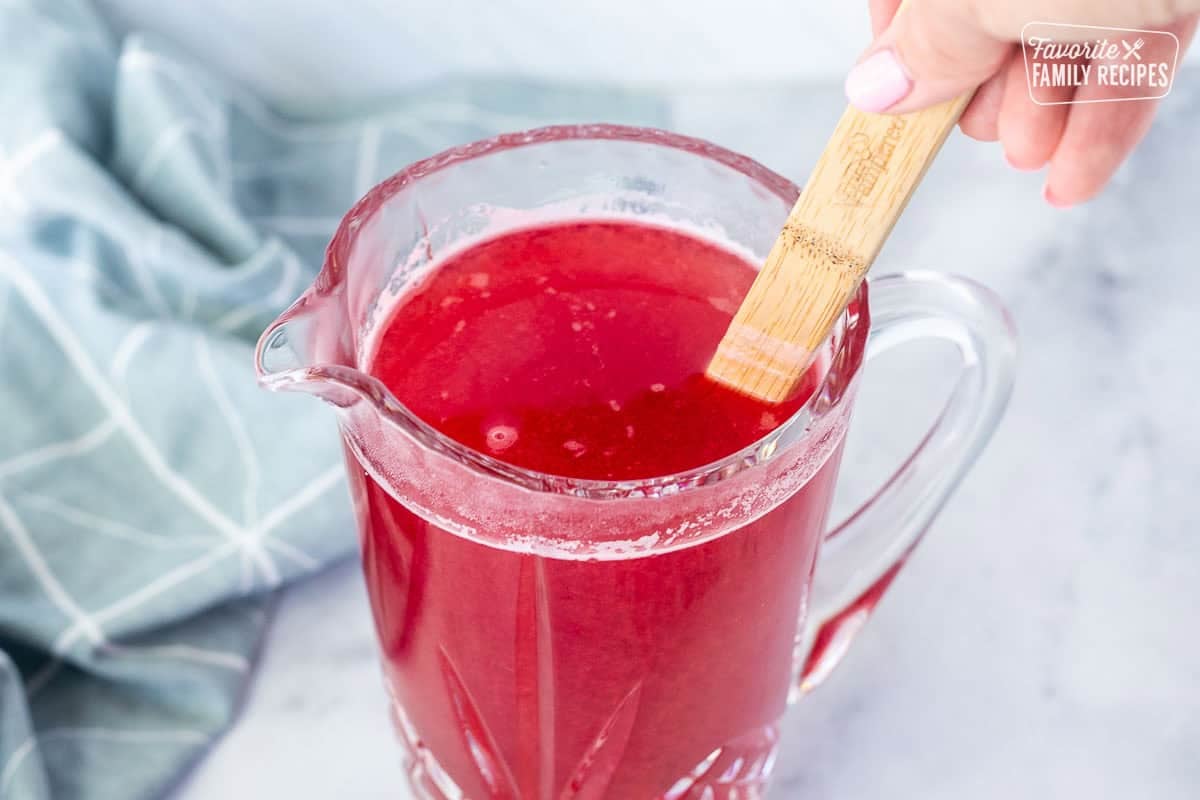 Stirring raspberry mixture together with water in a pitcher.