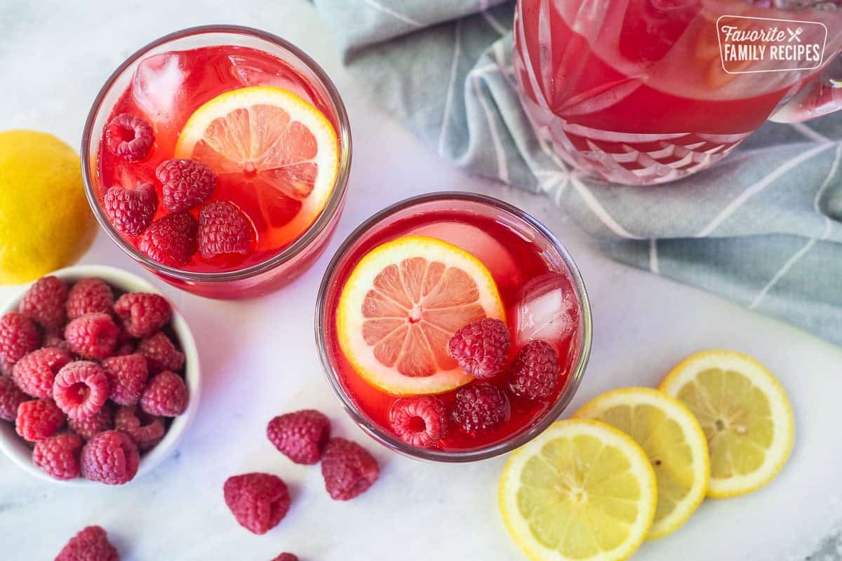 Glasses of raspberry cordial with ice, fresh lemon slice and fresh raspberries.