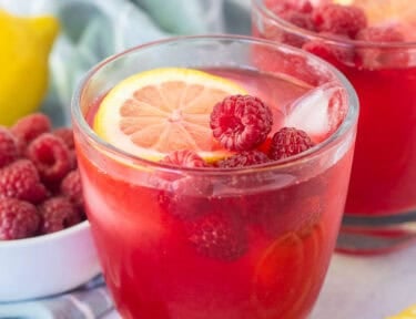 Glass of raspberry cordial with ice, fresh lemon slice and fresh raspberries.