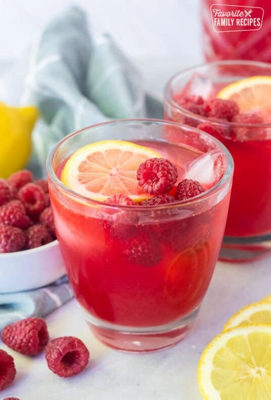 Glass of raspberry cordial with ice, fresh lemon slice and fresh raspberries.