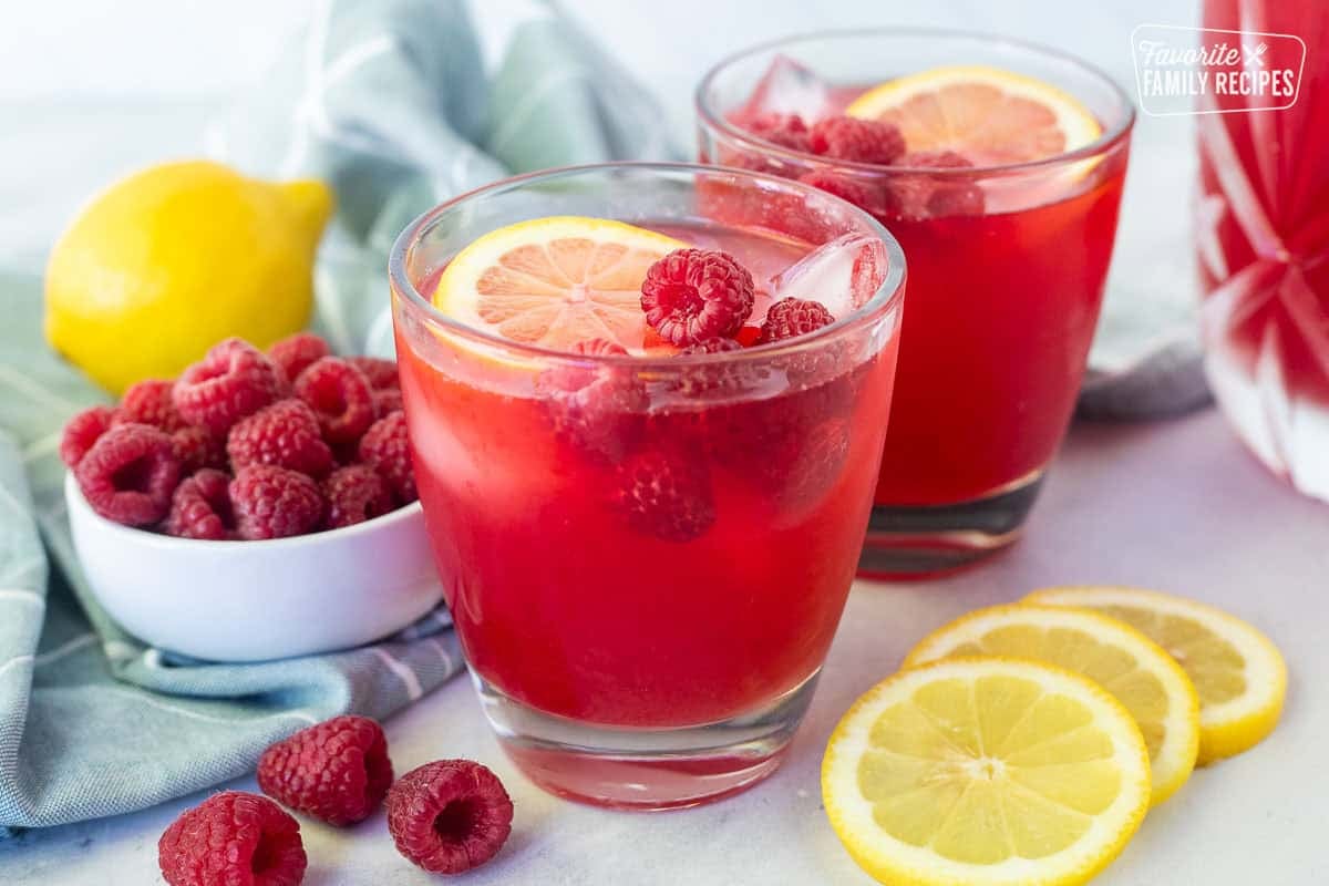 Glasses of raspberry cordial topped with fresh lemon slice and fresh raspberries.