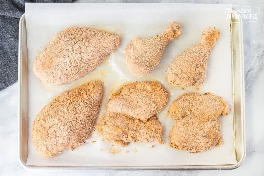 Pieces of chicken covered in breadcrumb mixture on a sheet pan.