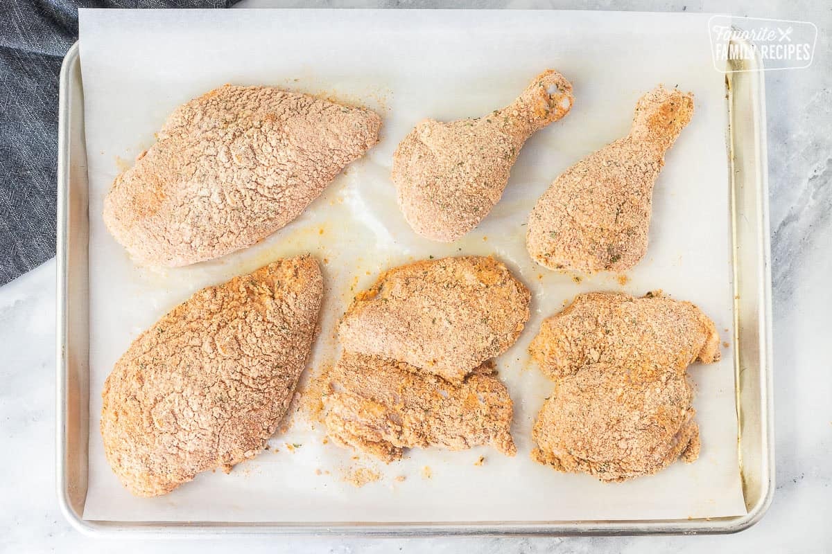 Pieces of chicken covered in breadcrumb mixture on a sheet pan.
