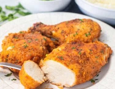 Cut piece of shake and bake chicken on a plate with a fork.