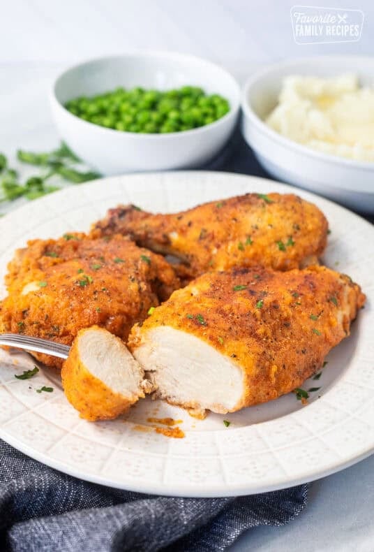Cut piece of shake and bake chicken on a plate with a fork.