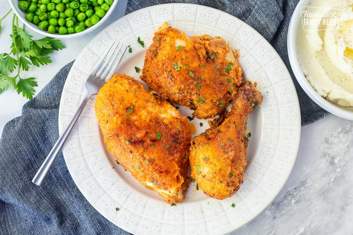 Shake and bake chicken pieces on a plate with a side of mashed potatoes and peas.