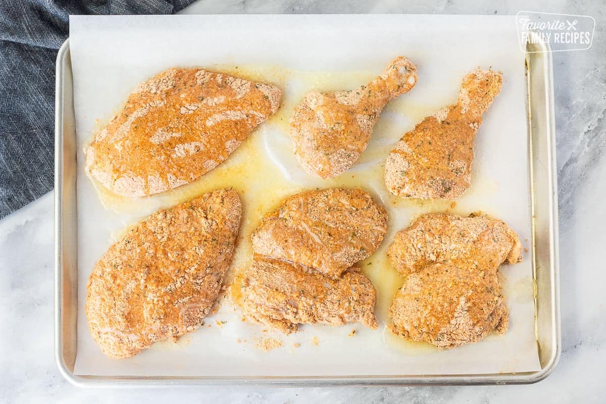 Sheet pan with chicken pieces coated with breadcrumb mixture and topped with butter oil.
