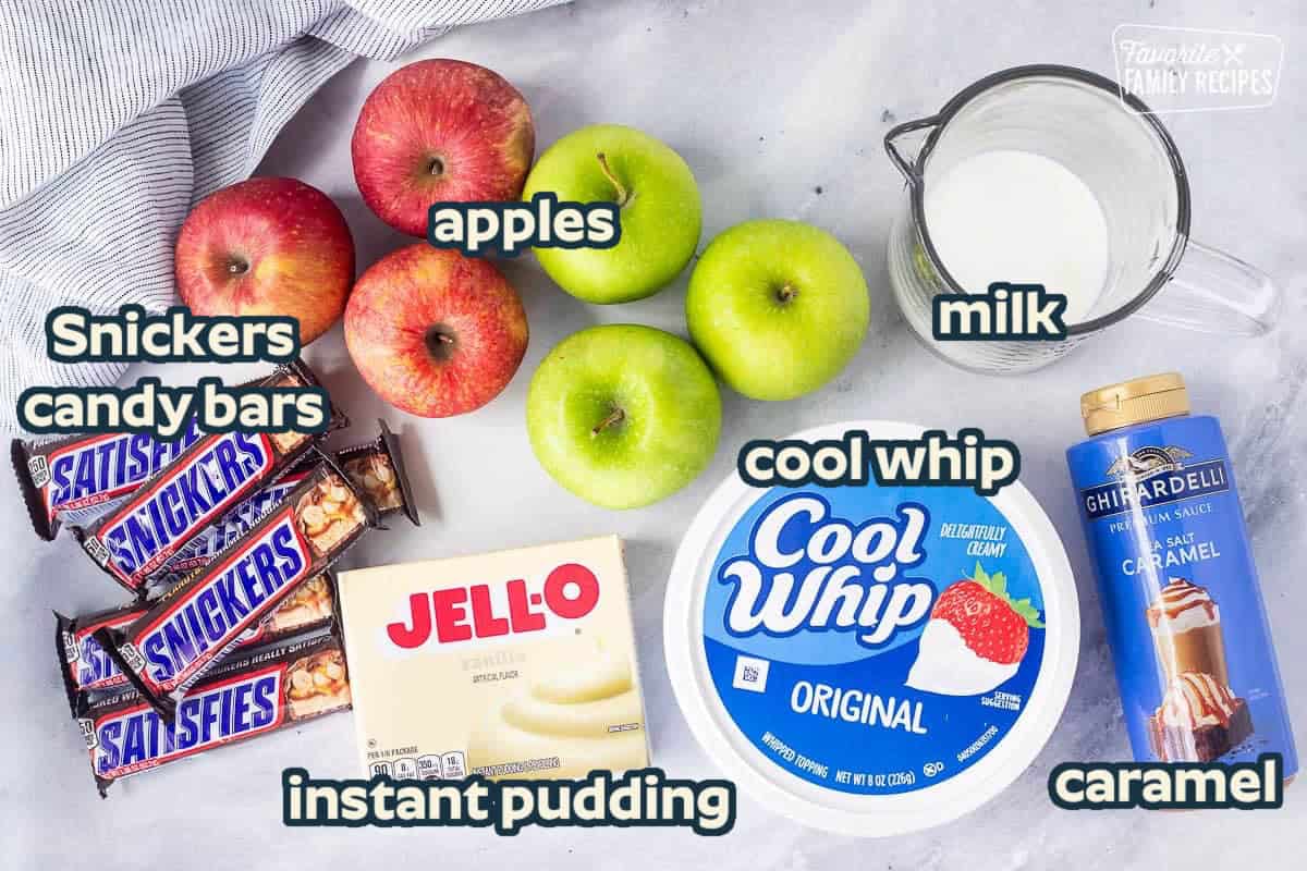 Ingredients to make Snickers Salad including jello vanilla instant pudding, milk, sea salt caramel, cool whip, snickers candy bars, green apples and red apples.