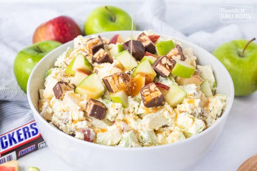 Pouring caramel sauce on top of Snickers Salad in a bowl.