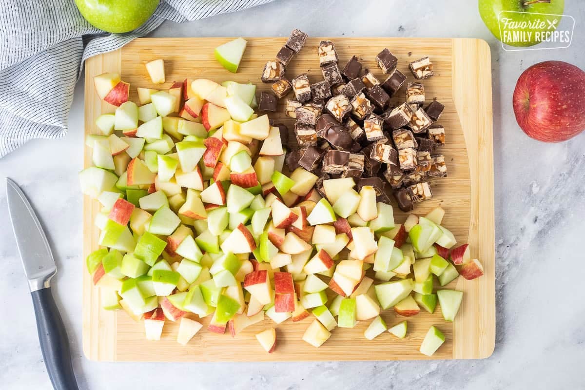 Cutting board with chopped apples and Snickers bars.