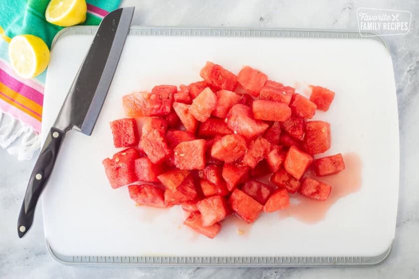Cutting board with cut watermelon pieces and a knife.