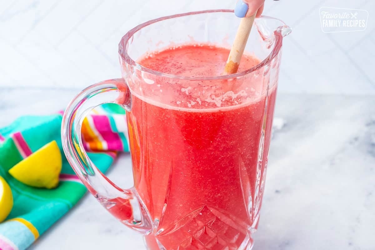 Stirring watermelon lemonade in a pitcher with a wooden spoon.