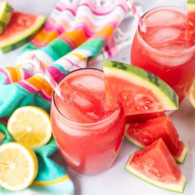 Glass of watermelon lemonade with a wedge of watermelon on the rim of the glass and a straw.