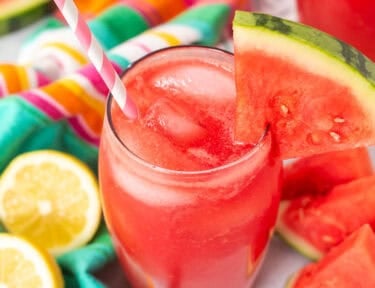 Glass of watermelon lemonade with a wedge of watermelon on the rim of the glass and a straw.