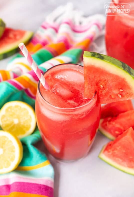 Glass of watermelon lemonade with a wedge of watermelon on the rim of the glass and a straw.