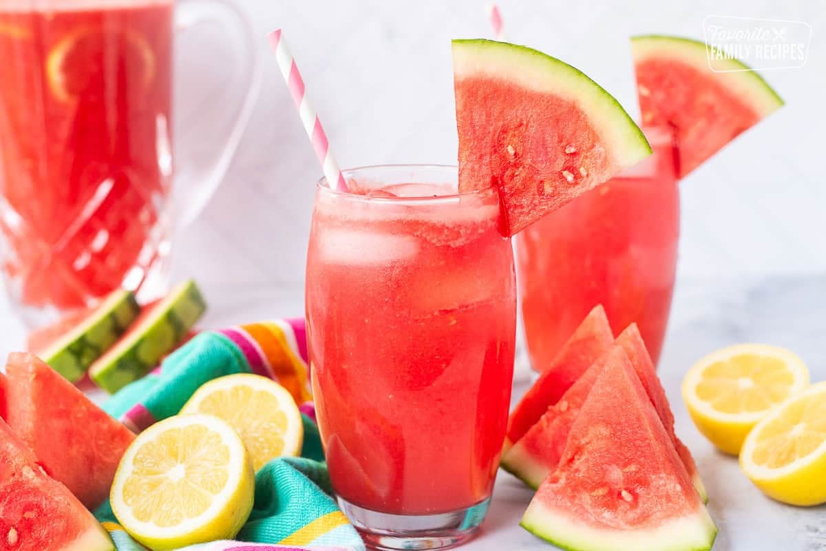 Two glasses of watermelon lemonade with a wedge of watermelon on the rim of the glass and a straw.