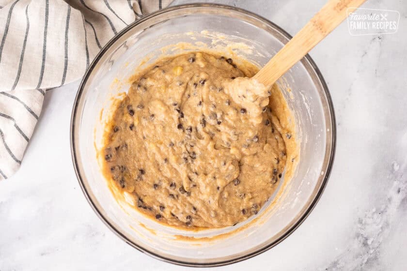 Glass mixing bowl of banana chocolate chip muffin batter and wooden spoon.