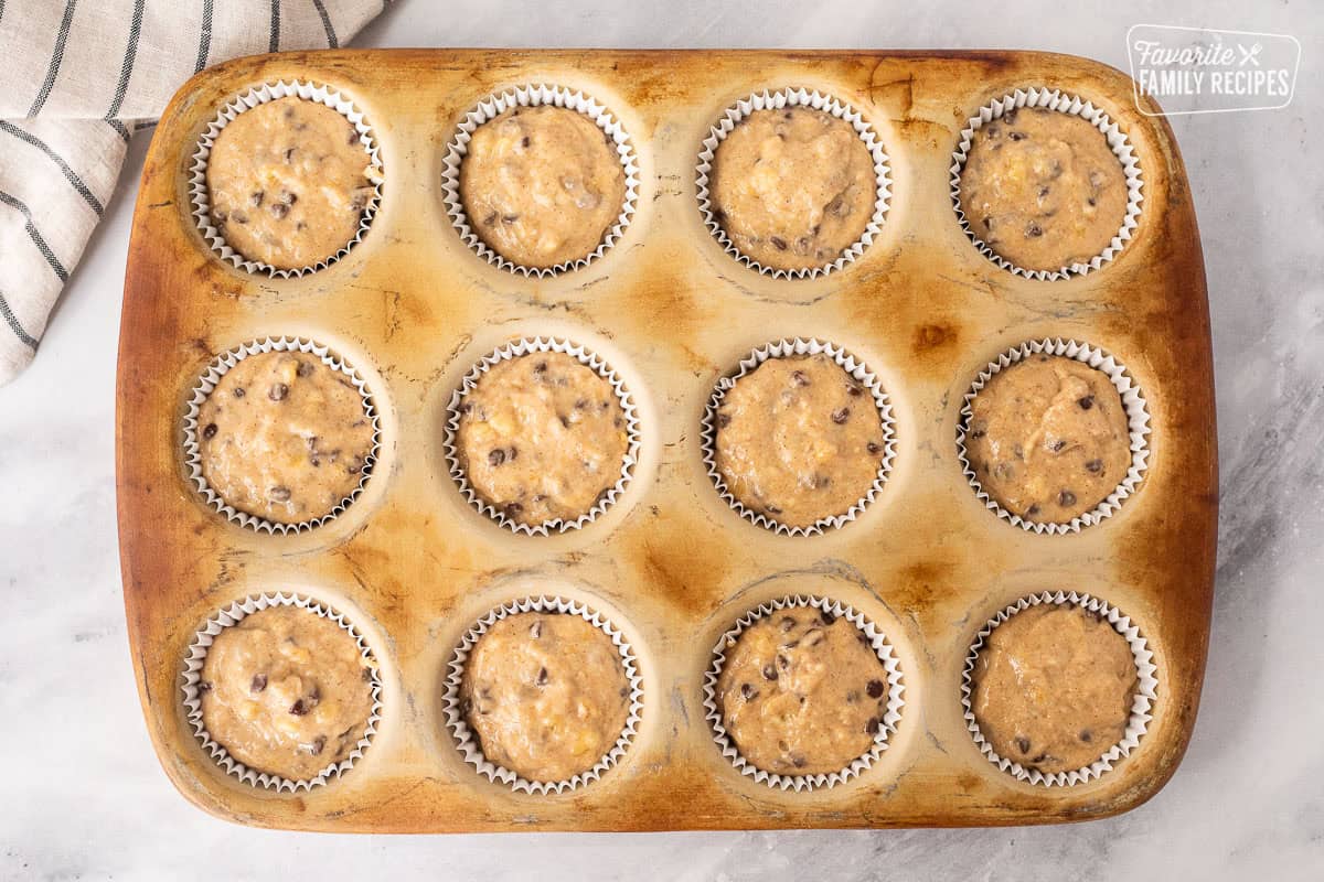 Banana chocolate chip muffin batter in muffin liners of a muffin pan.