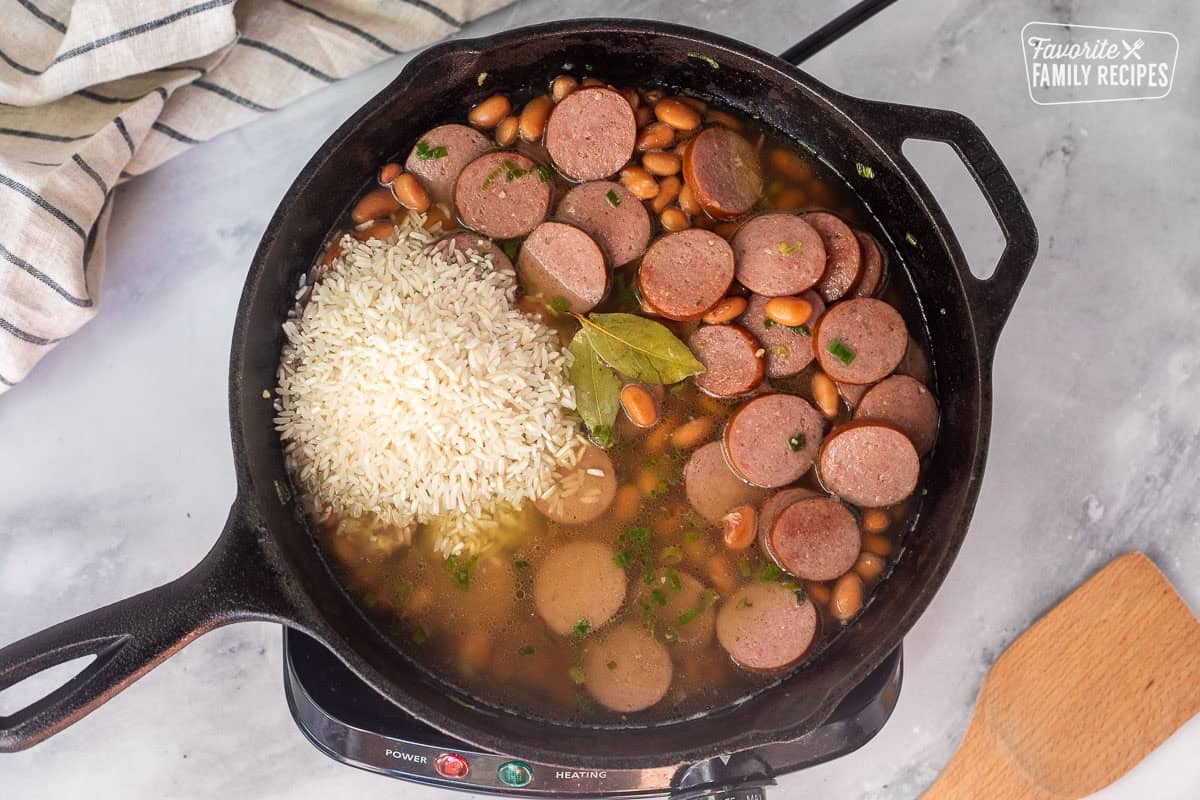 Adding broth, rice and bay leaves to a skillet with sausage and pinto beans.