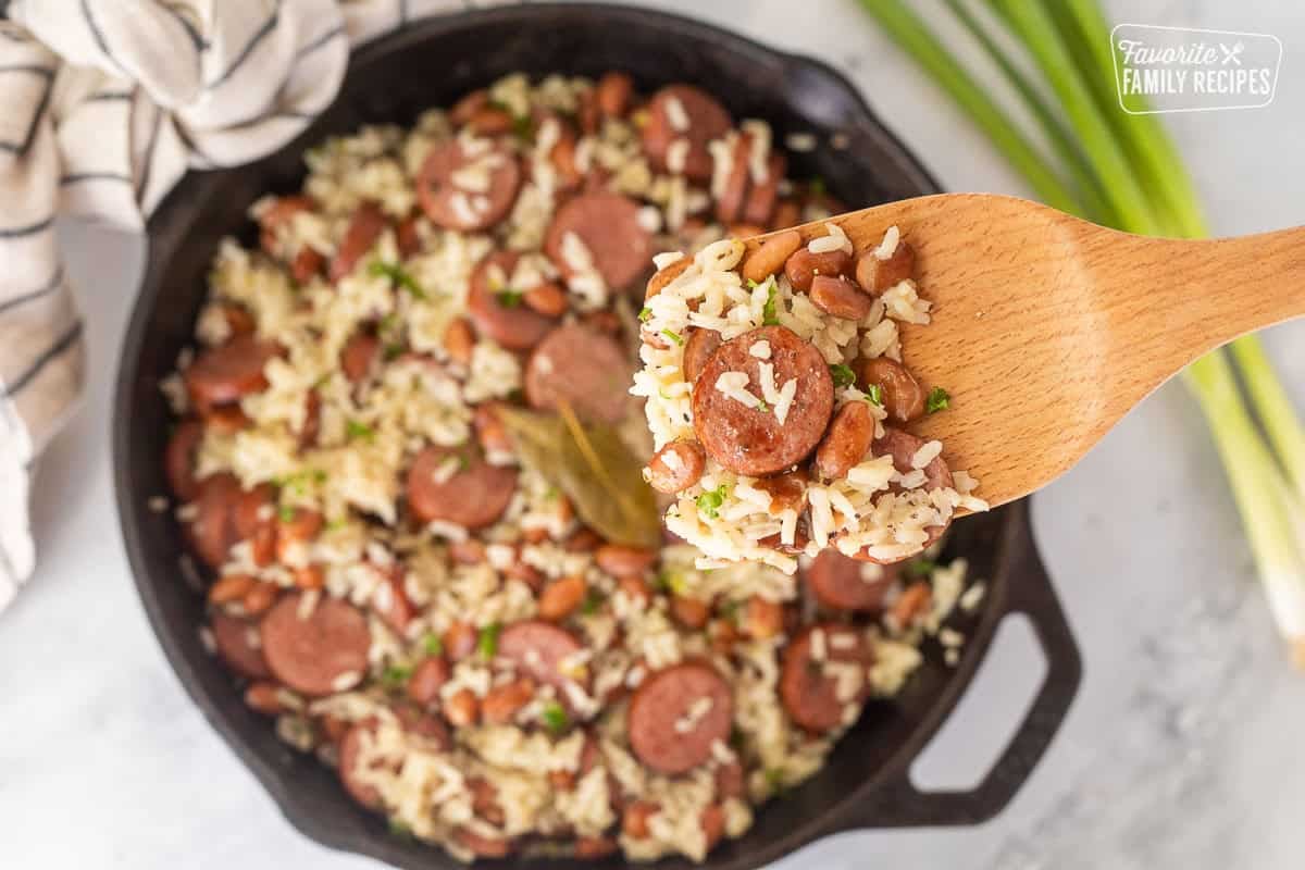 Wooden spoon with a scoop of Brazilian rice and beans over s skillet.