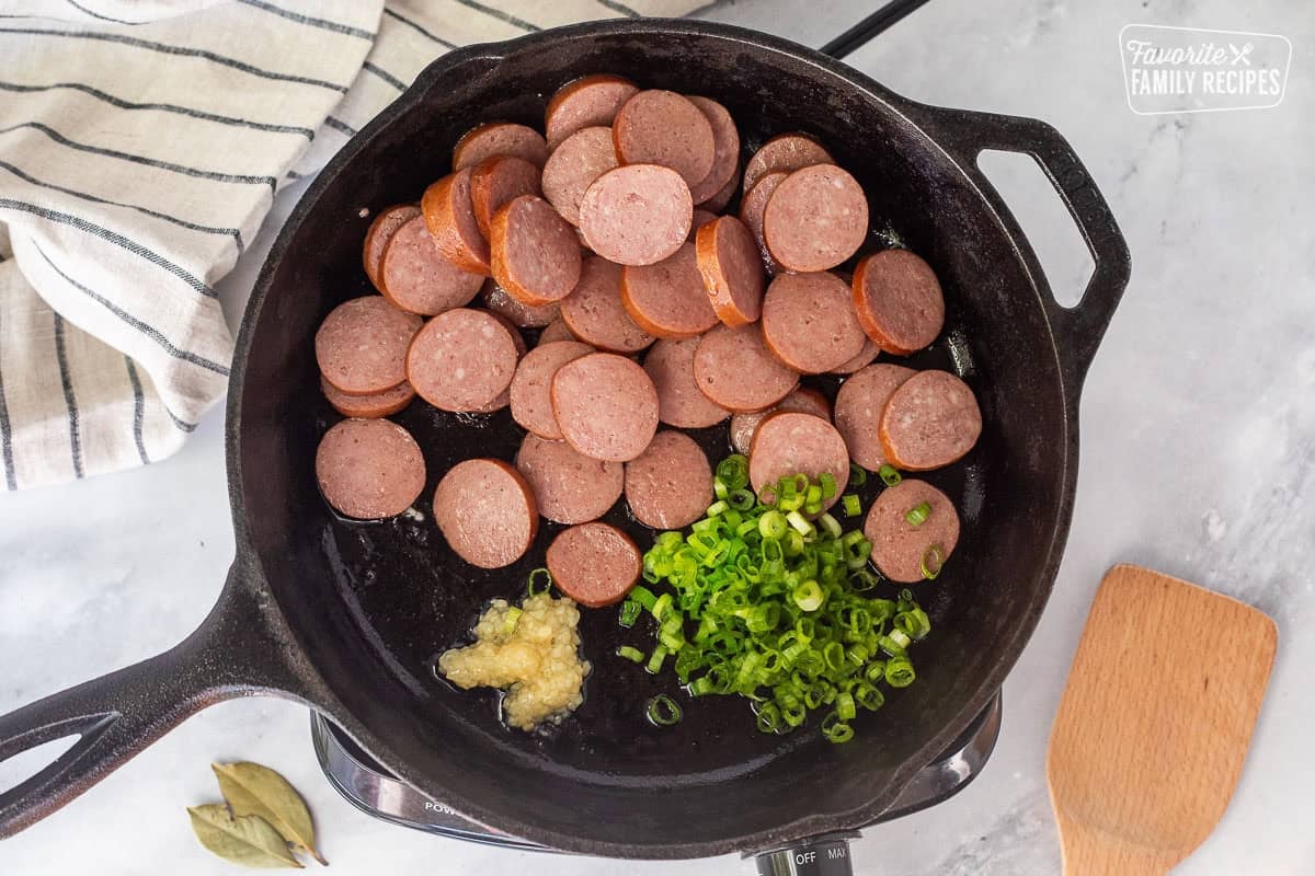 Skillet with sliced sausage, green onion and garlic in a hot skillet.