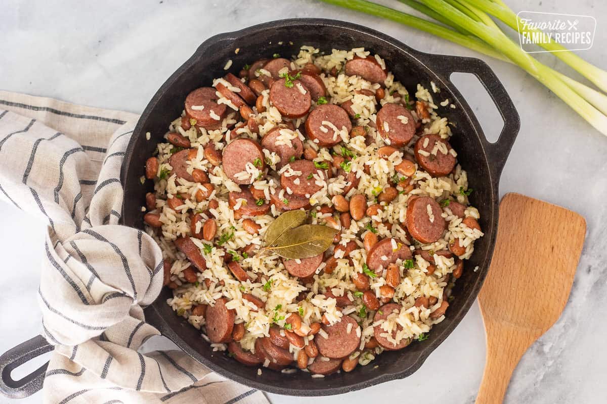 Cooked Brazilian rice and beans in a skillet garnished with parsley and wooden spoon on the side.