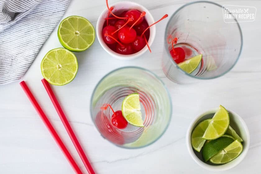 Two glasses with a lime wedge and cherry on the bottom.