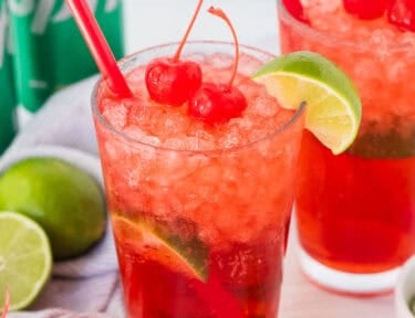 Two glasses of cherry limeade and garnished with cherries and a lime wedge.