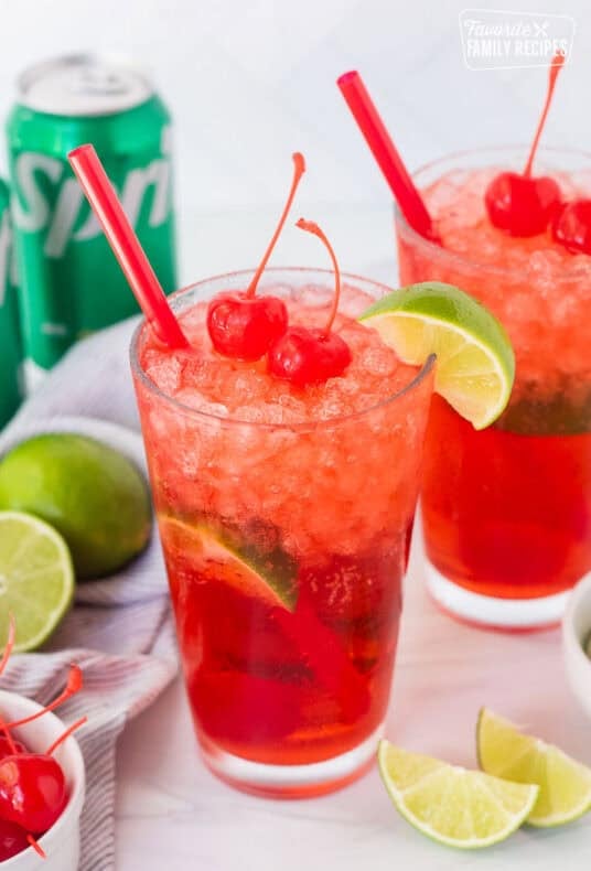 Two glasses of cherry limeade and garnished with cherries and a lime wedge.