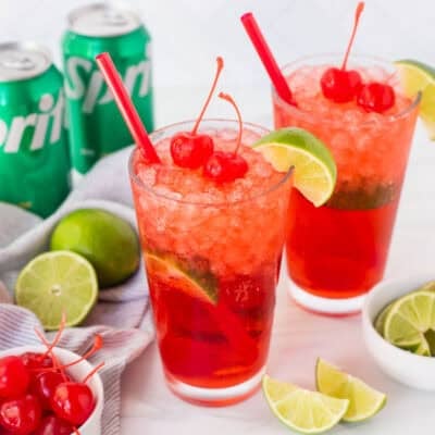 Two glasses of cherry limeade and garnished with cherries and a lime wedge.