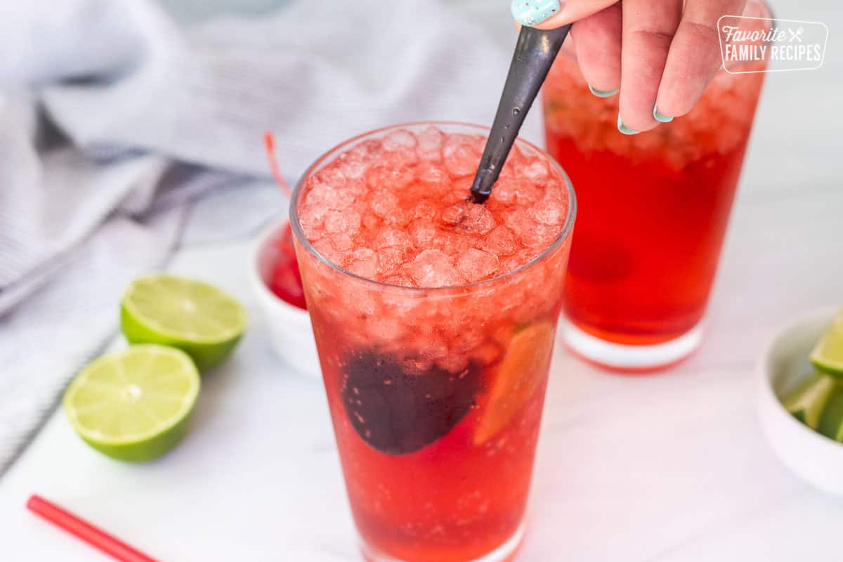 Stirring cherry syrup and Sprite for cherry limeade in a glass with a spoon.