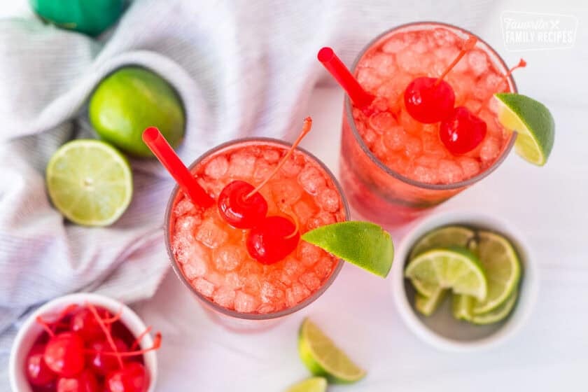 Glasses of cherry limeade and garnished with cherries and a lime wedge.