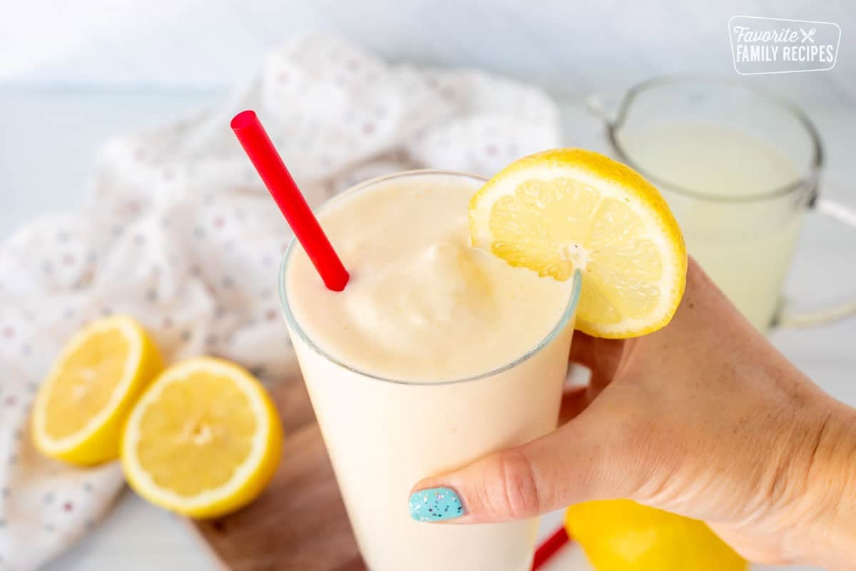 Hand holding a glass of Chick-Fil-A frosted lemonade with a lemon slice and a straw.