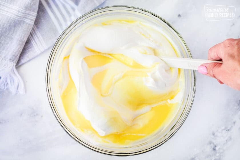 Milk, instant vanilla pudding, and Cool whip mixed together in a bowl for an eclair cake filling