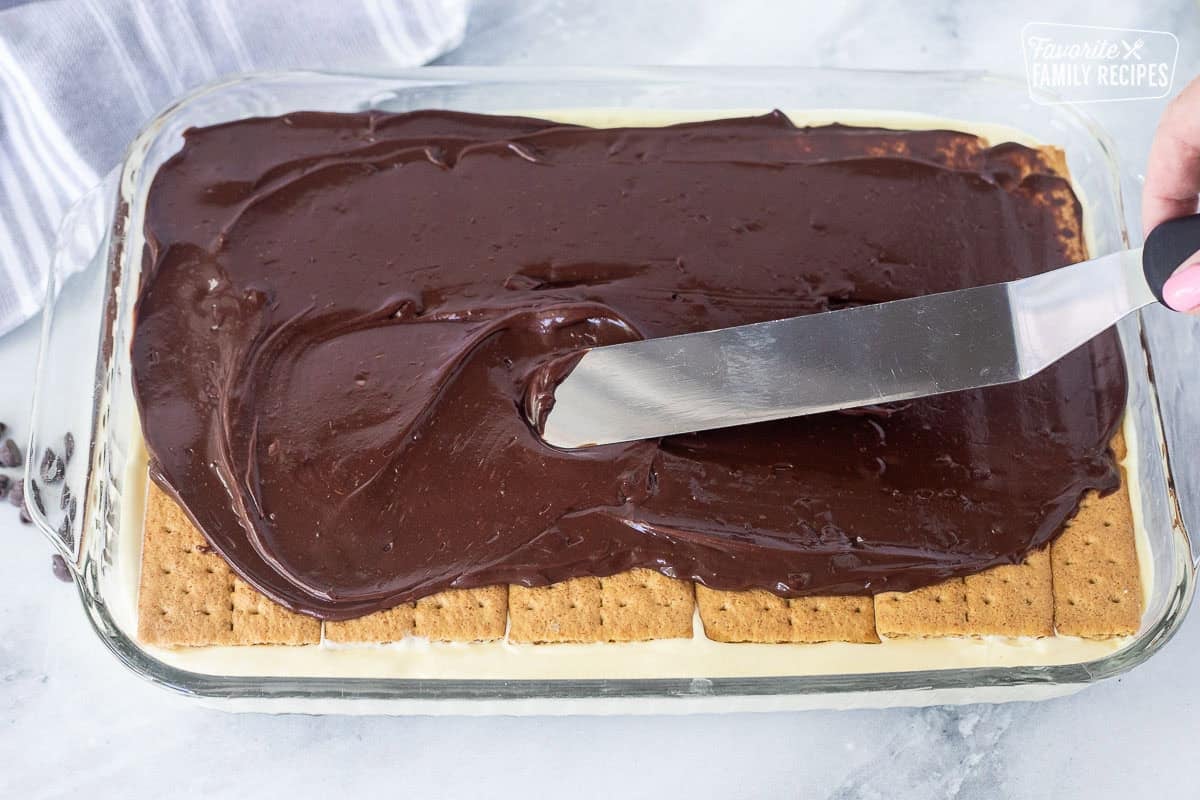 Smooth chocolate ganache spread over the top layer of graham crackers on a chocolate eclair cake