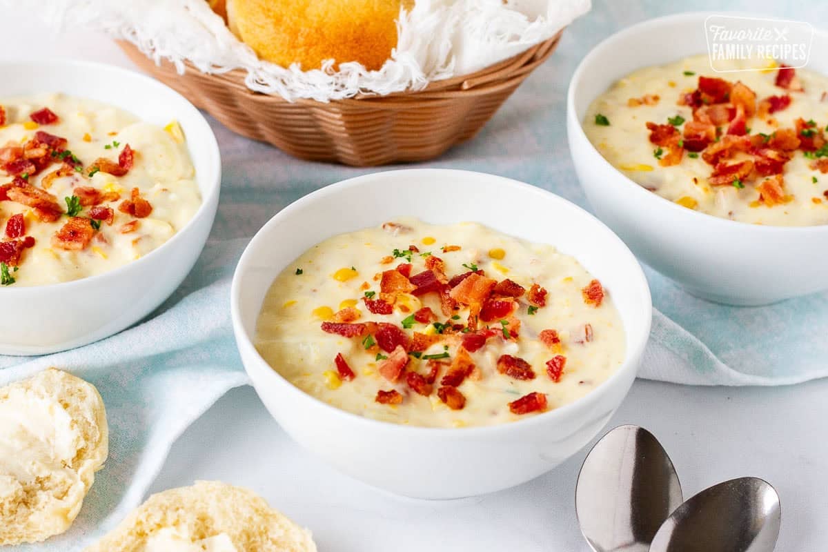 Bowls of corn chowder with bacon topped with extra bacon and parsley. Dinner rolls on the side.