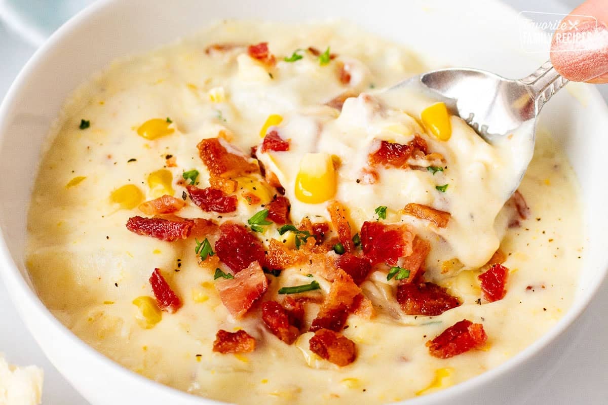 Spoon scooping from a bowl of corn chowder with bacon.