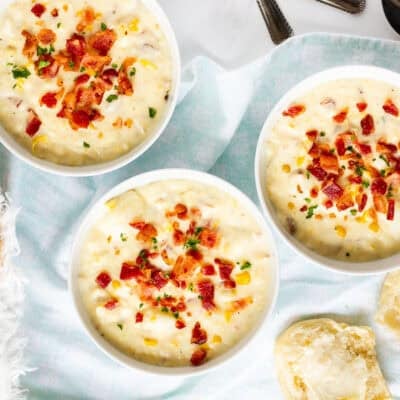 Three bowls of corn chowder with bacon topped with extra bacon and parsley. Dinner rolls on the side.