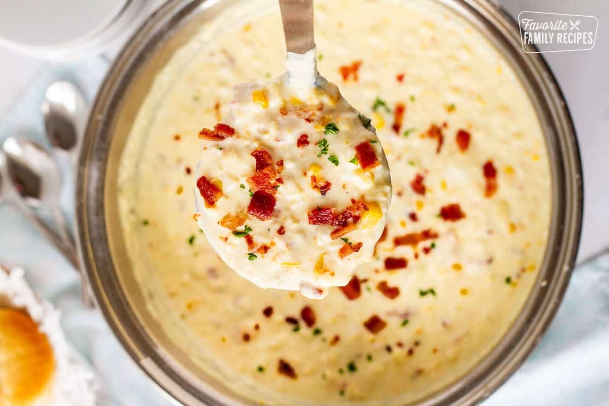 Large pot of corn chowder with bacon with a ladle full of soup.