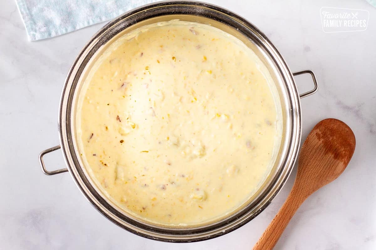 Large pot of corn chowder with bacon with wooden spoon on the side.
