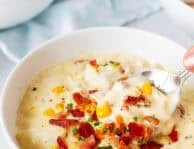 Spoon scooping from a bowl of corn chowder with bacon.