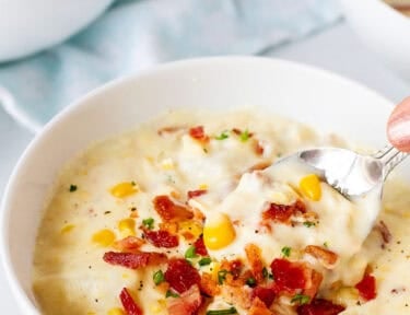 Spoon scooping from a bowl of corn chowder with bacon.