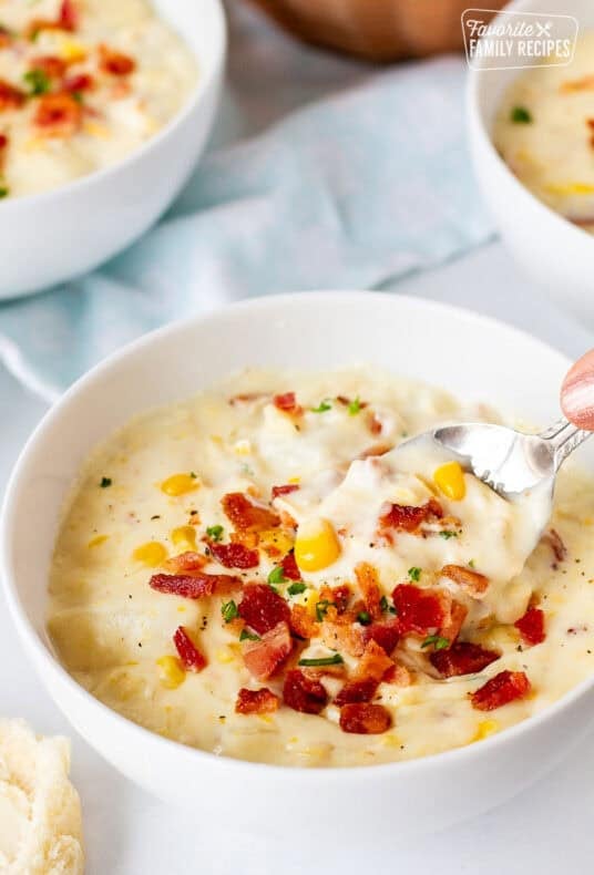 Spoon scooping from a bowl of corn chowder with bacon.
