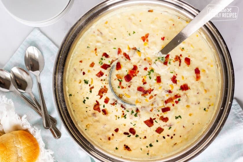 Large pot of corn chowder with bacon and a ladle full of soup.