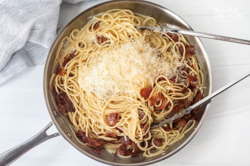 Skillet and tongs with carbonara sauce, spaghetti, bacon and Parmigiana Reggiano.