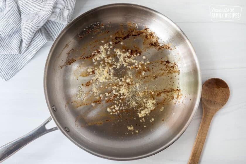Skillet with bacon grease cooking garlic.