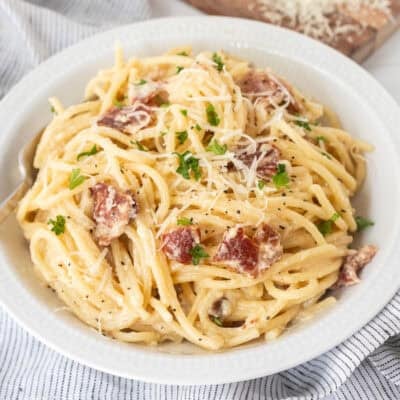 Bowl of creamy carbonara serving with fresh grated cheese and parsley on top.