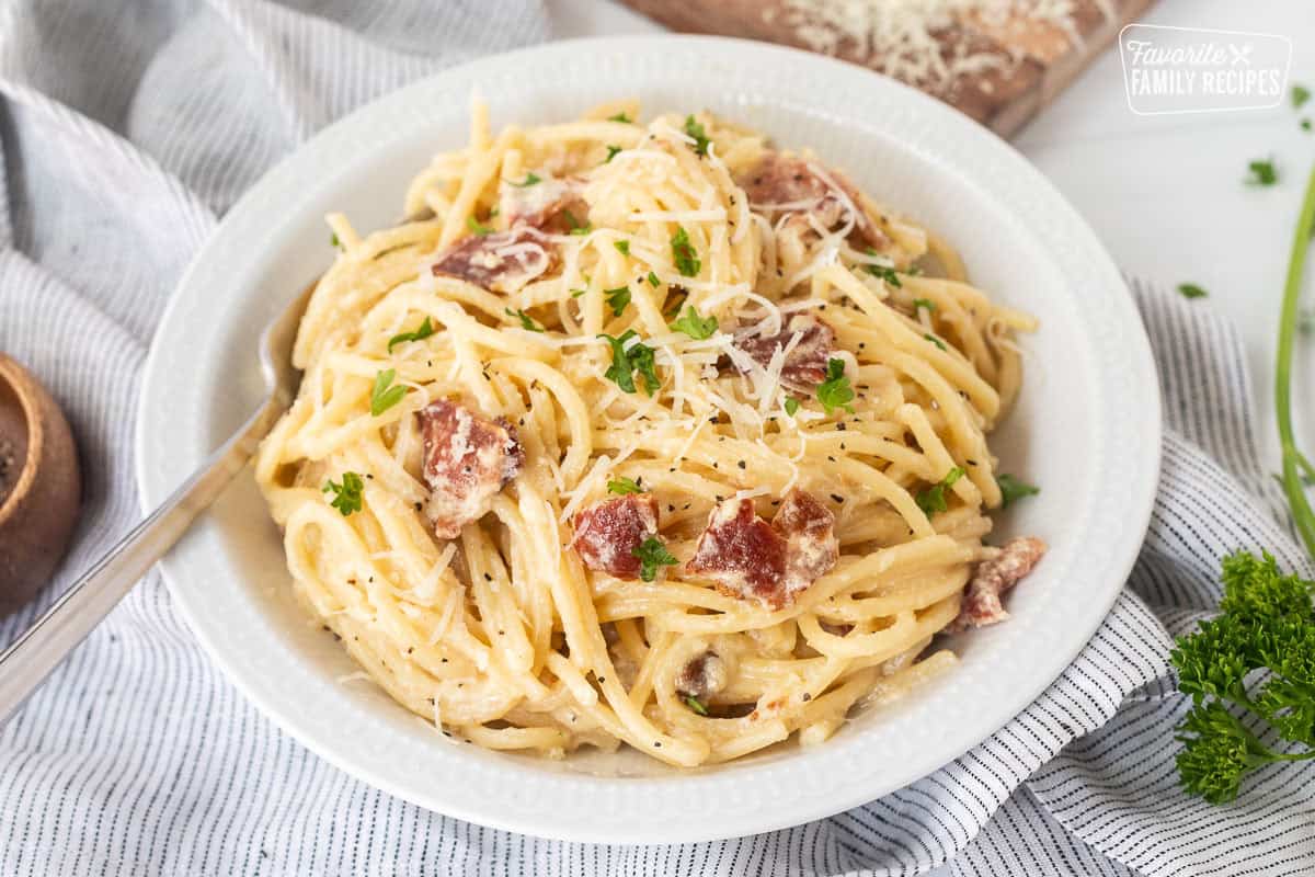 Bowl of creamy carbonara serving with fresh grated cheese and parsley on top.