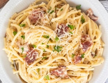 Bowl of creamy carbonara serving with fresh grated cheese and parsley on top.