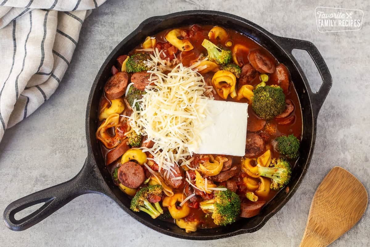 Adding cream cheese and parmesan cheese to skillet of tortellini with sausage.